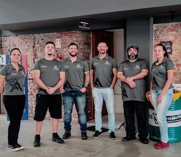 Equipe da AuttoMotive, seis pessoas com a camiseta da marca, na frente da oficina